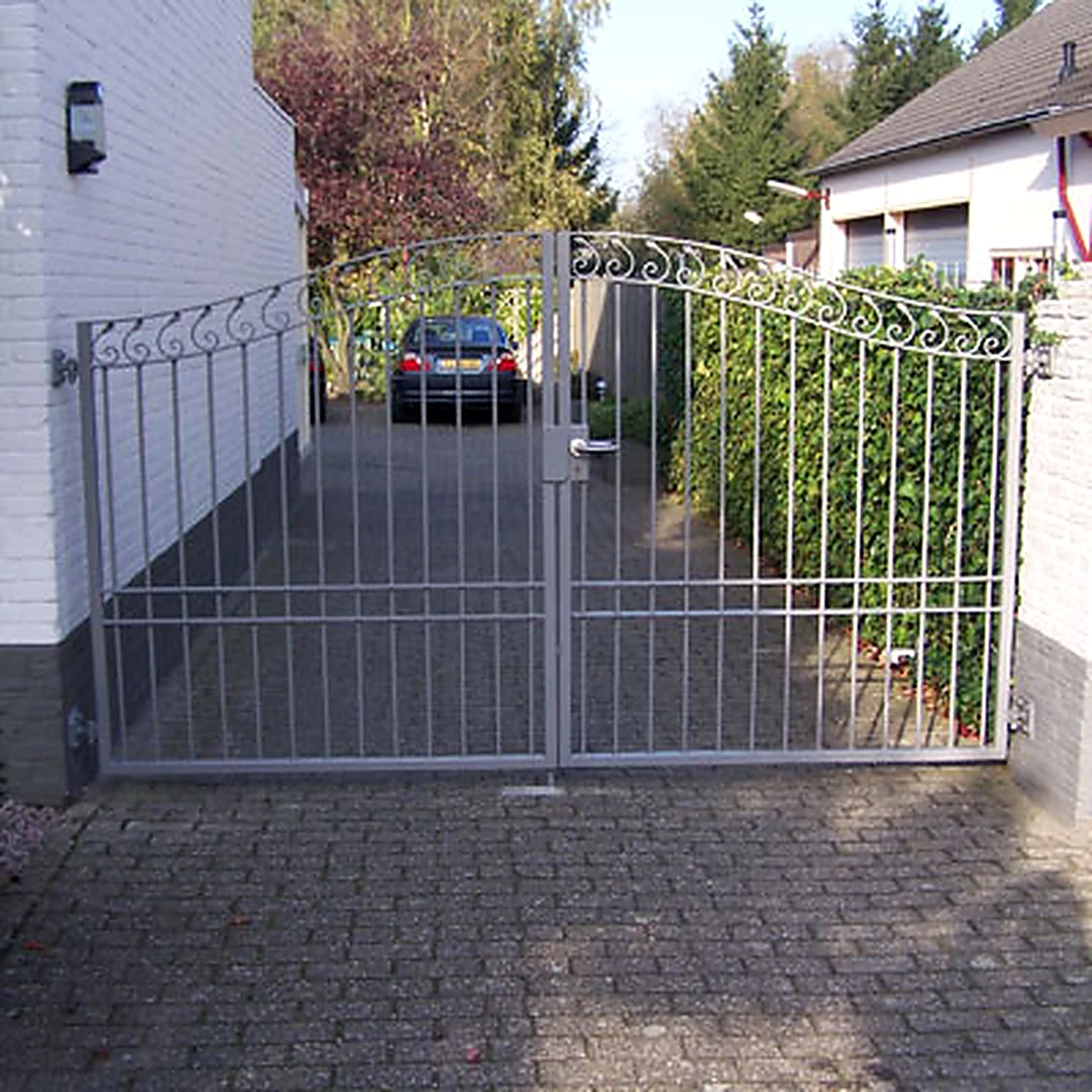 Dubbele stalen opritpoort met sierkrullen en gebogen bovenzijde in Gemonde.